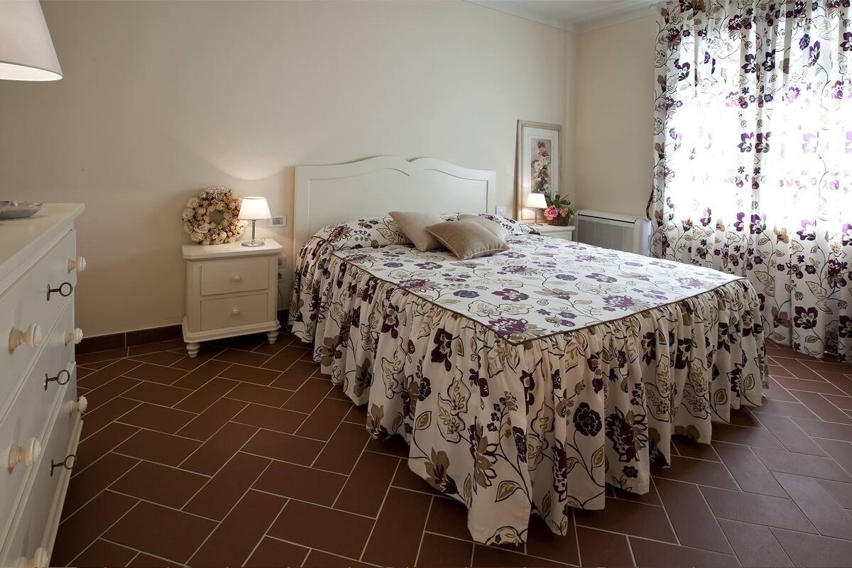 A bedroom with a bed, nightstands, a dresser, and a window with curtains.