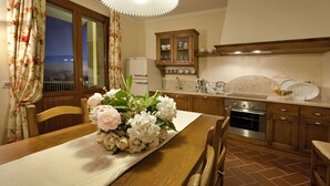 A dining area with a wooden table, chairs, a floral centerpiece, and a kitchen in the background. - Tenuta Quadrifoglio (Gambassi Terme)