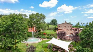 A landscaped garden with a fountain, outdoor seating, and a stone building. - Tenuta Quadrifoglio (Gambassi Terme)