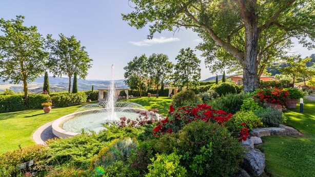 A well-maintained garden with a central fountain, surrounded by lush greenery and flowering plants. - Tenuta Quadrifoglio (Gambassi Terme)