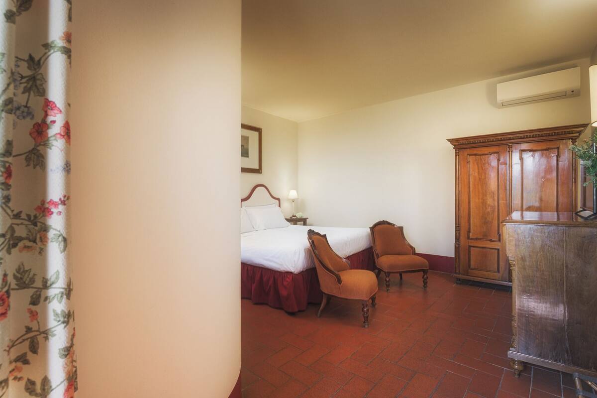 Habitación de hotel con una cama, dos sillas, un armario de madera y un equipo de aire acondicionado.