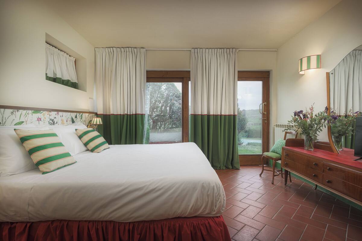 Un dormitorio con cama, cómoda, espejo y ventana con cortinas.