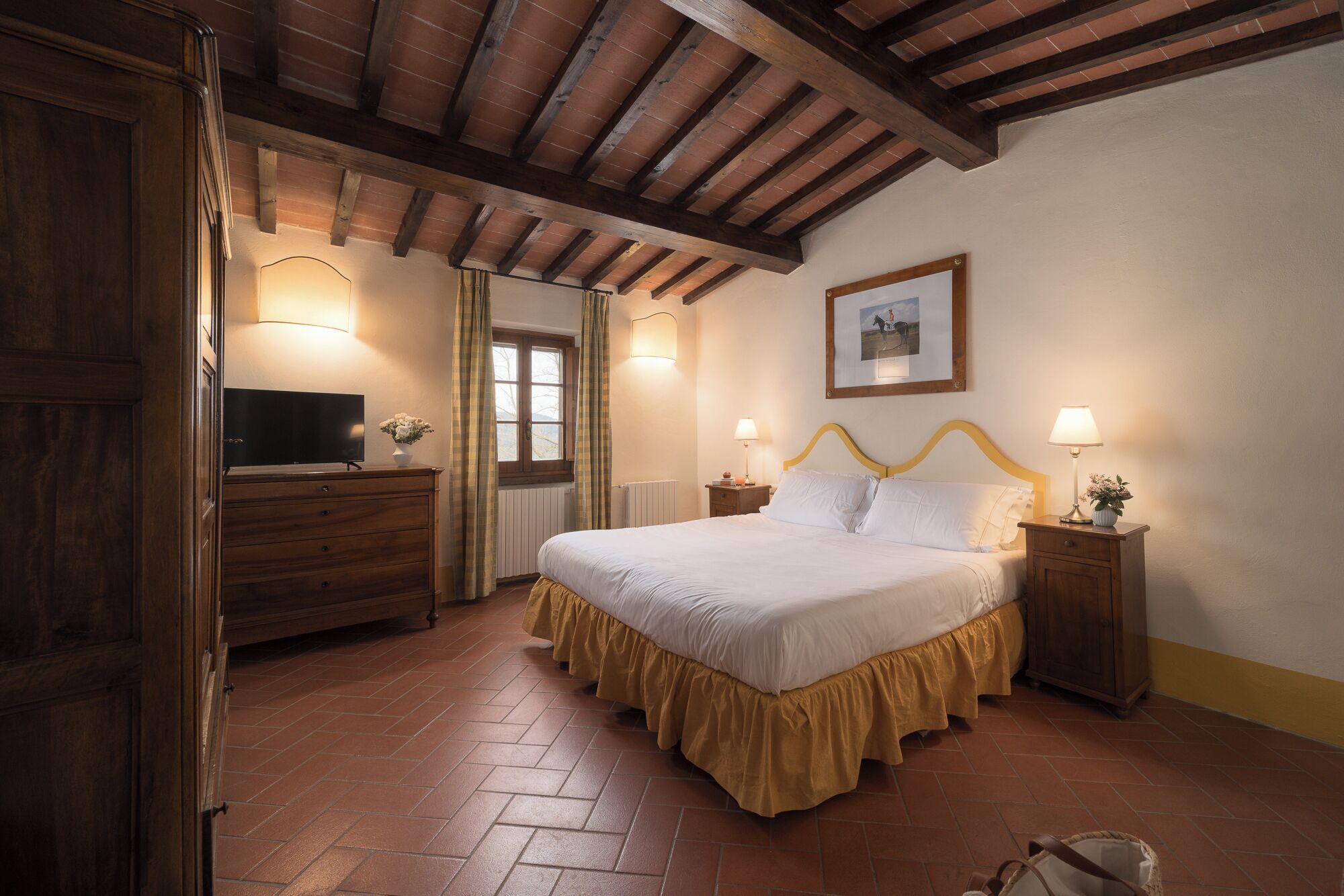 Une chambre à coucher avec un lit en bois, une commode, un téléviseur et une fenêtre avec des rideaux.