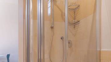 A glass-enclosed shower with a handheld showerhead and a towel rack.