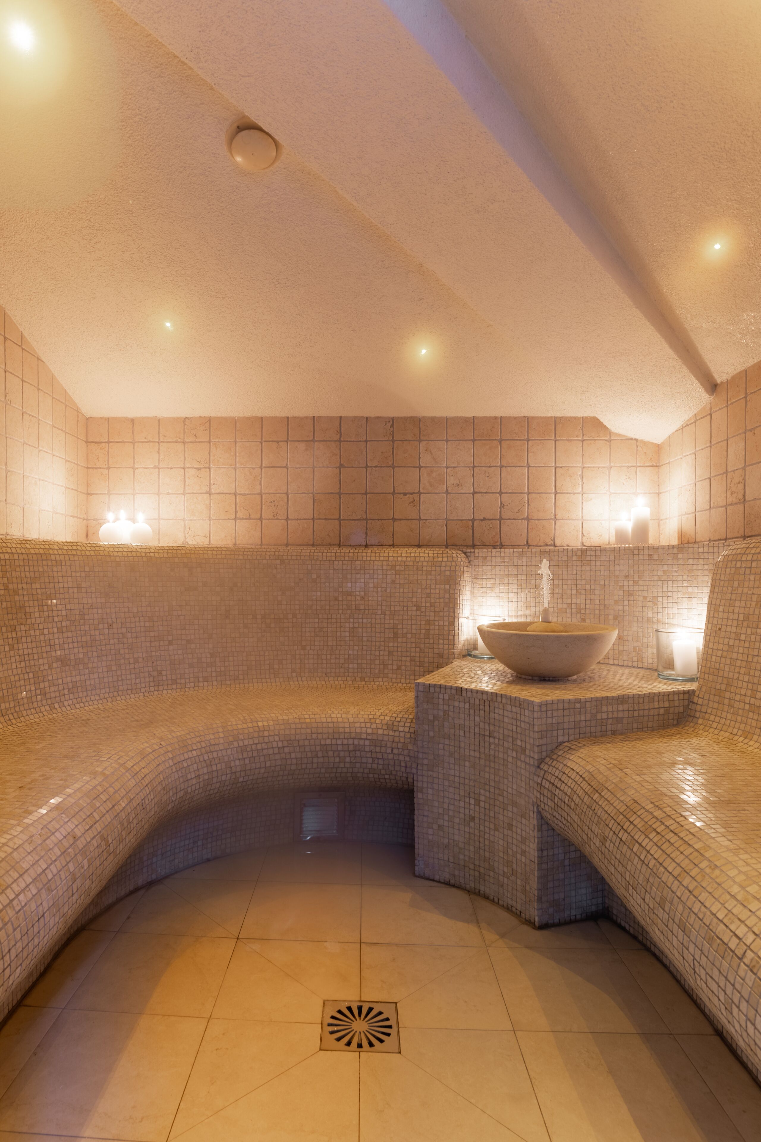 Un cuarto de spa con una zona de estar curva, un recipiente central e iluminación en la pared.