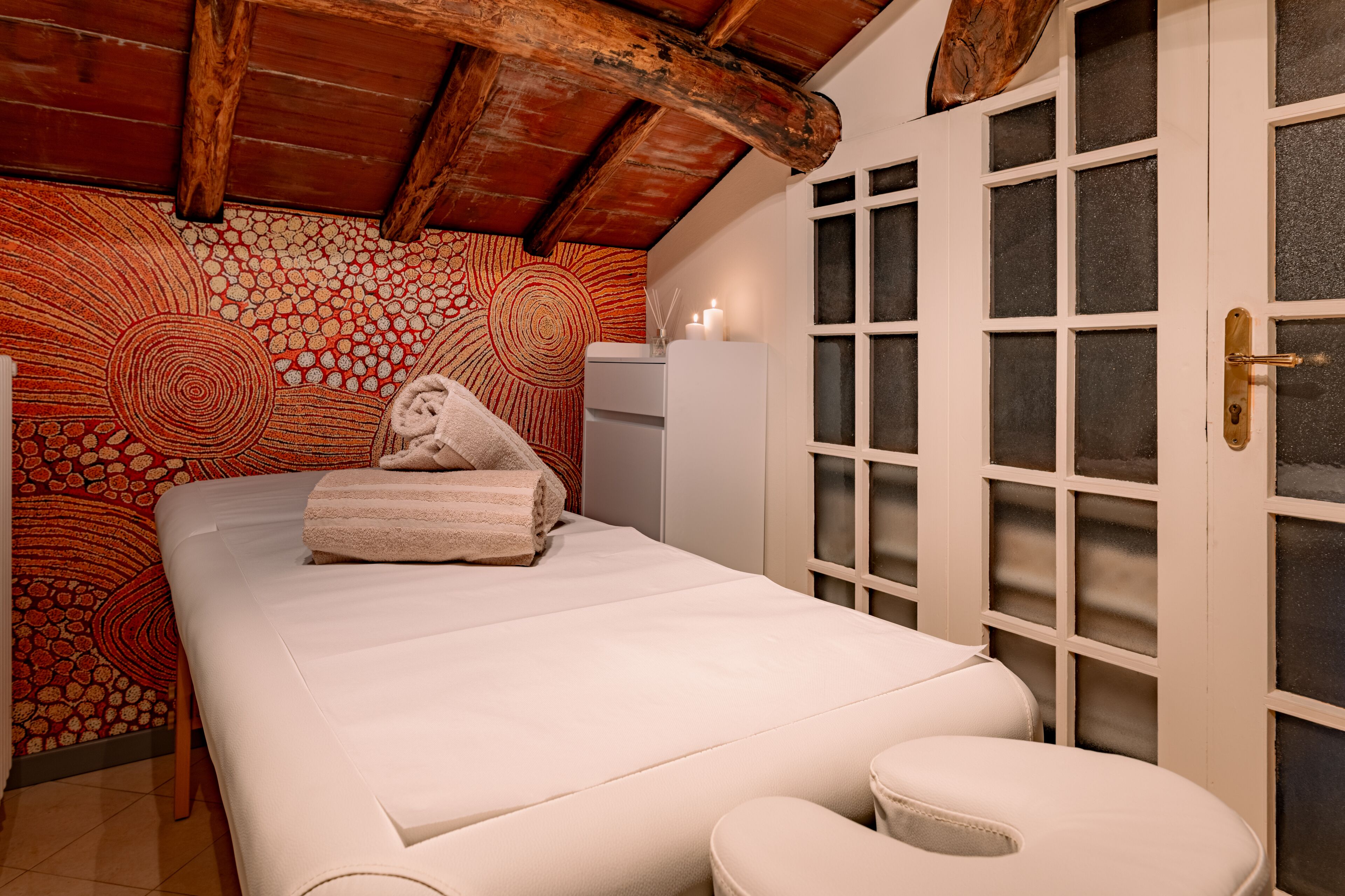 A room with a bed, a small table, a chair, and a door with frosted glass panels.
