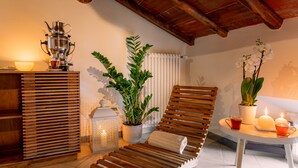 Una stanza luminosa con una poltrona in legno, un tavolo con una candela, una pianta in vaso e un set da tè tradizionale.