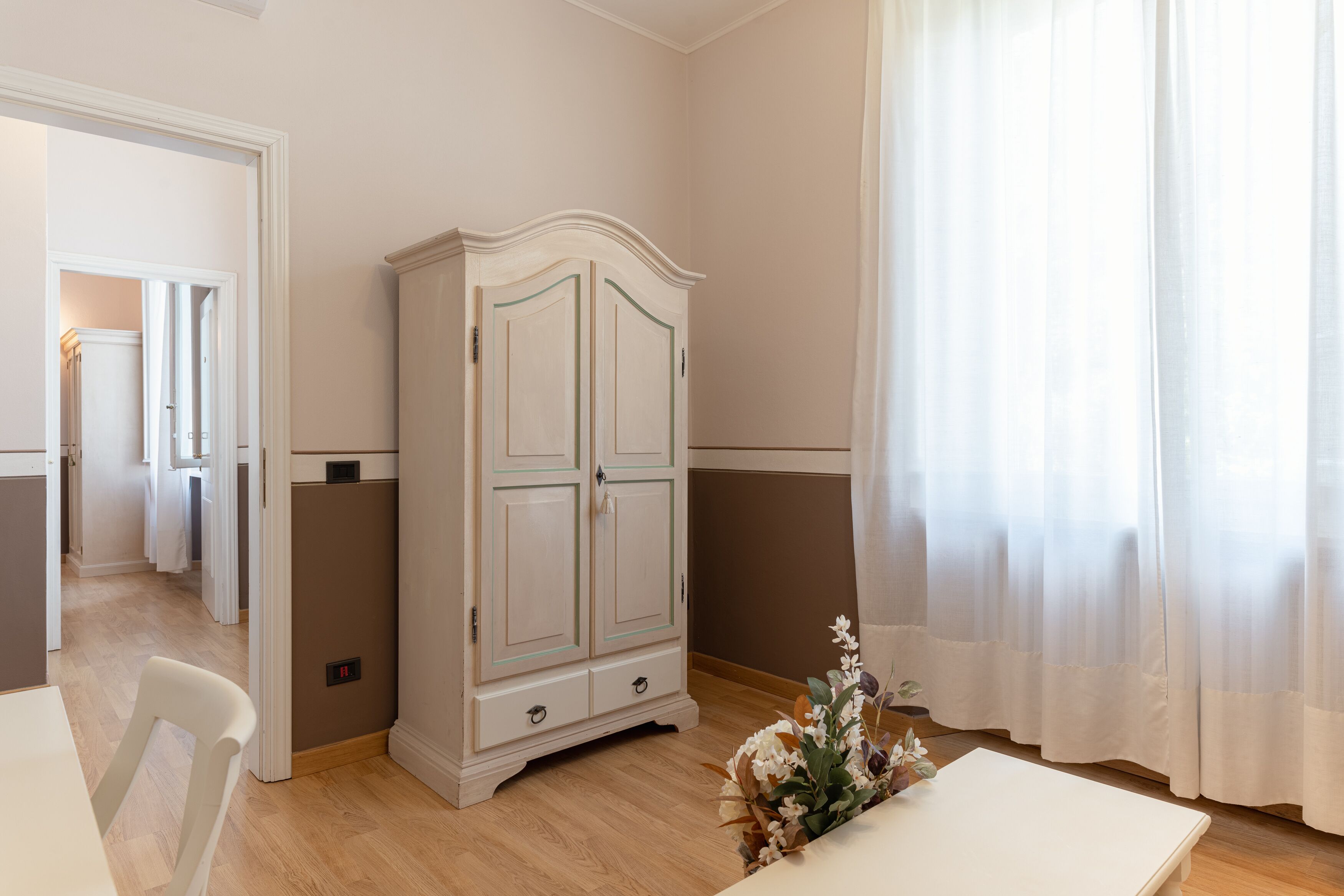 A room with a white cabinet, a table, and a chair. There is a door leading to another room.