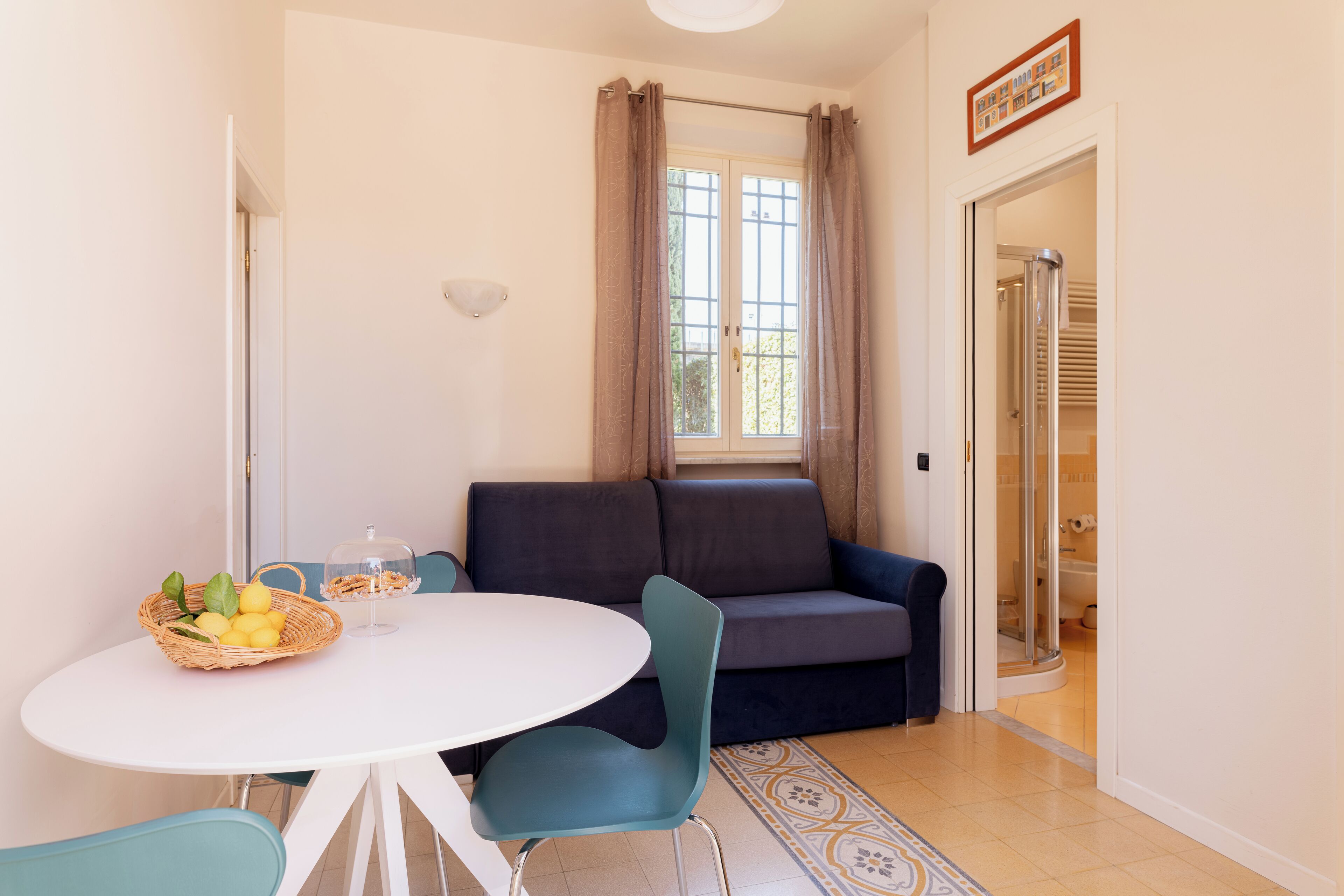 A compact living space with a round dining table, a sofa, a glass shower enclosure, and a patterned rug.