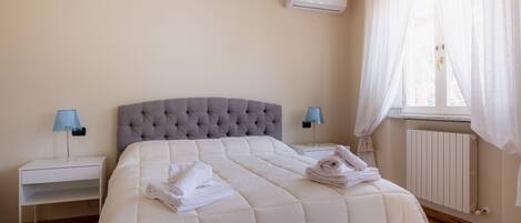 A neatly made bed with a grey headboard, two bedside tables with lamps, and a window with curtains.