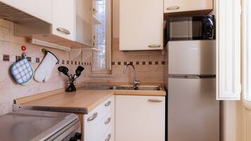 A compact kitchen with a stove, microwave, sink, and white cabinets.