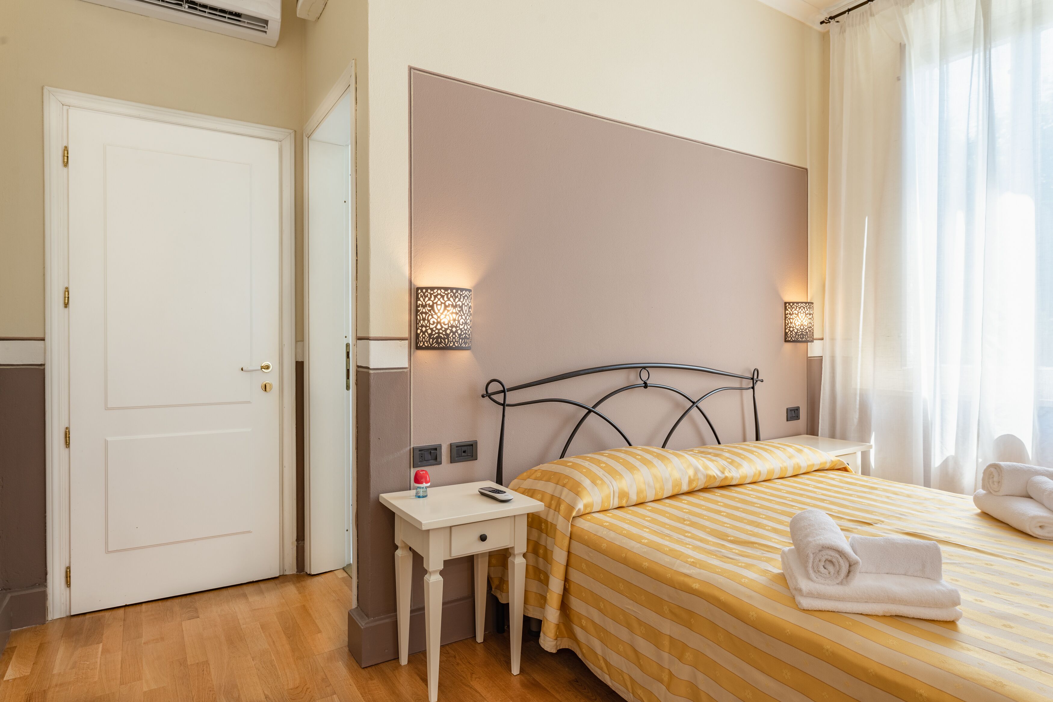 A hotel room with a bed, bedside table, lamp, and a door.