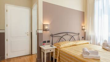 A hotel room with a bed, bedside table, lamp, and a door.