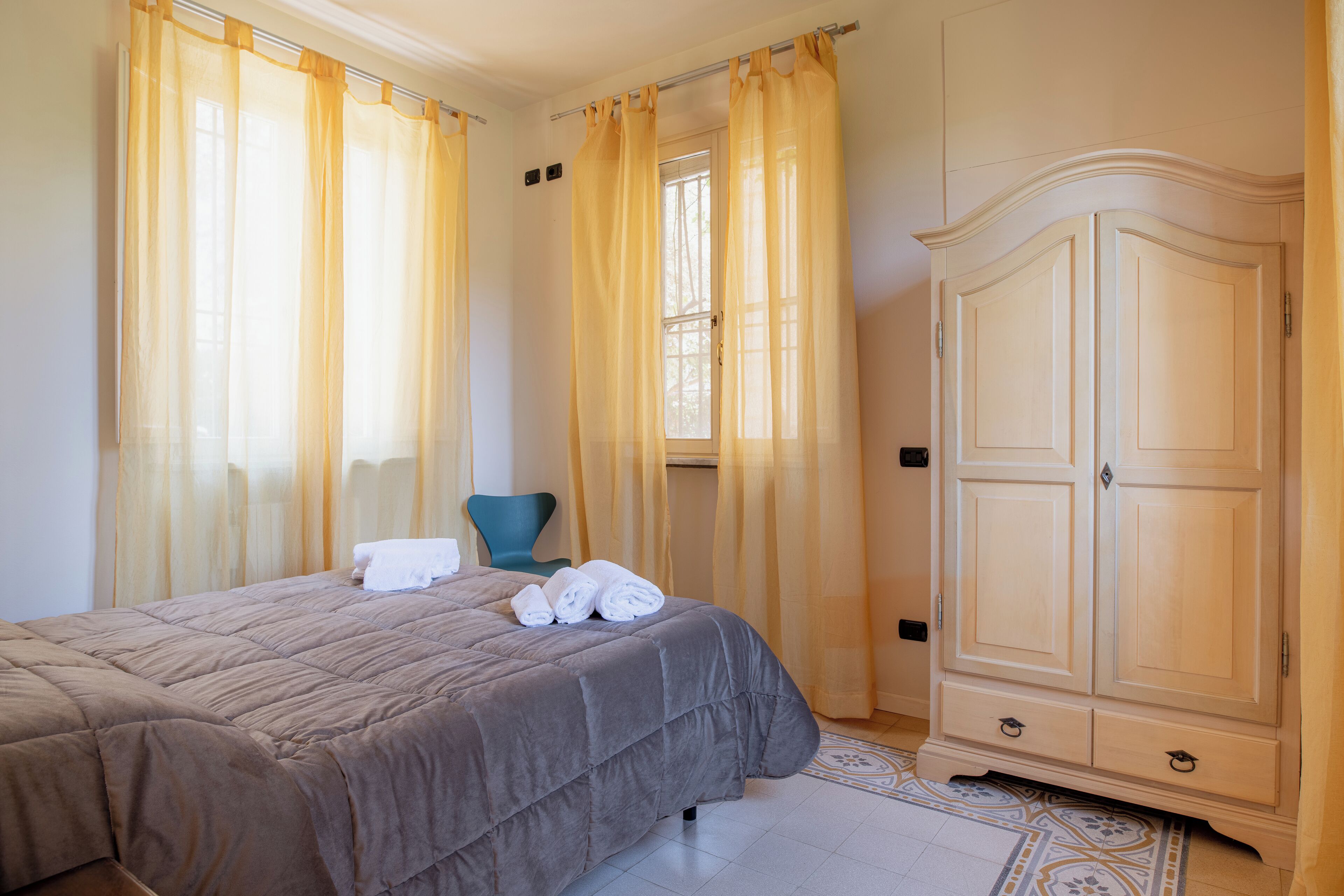 Ein Schlafzimmer mit Bett, Stuhl, Schrank und einem Fenster mit Vorhängen.
