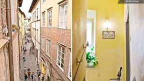 Une rue étroite, bordée de bâtiments des deux côtés, une enseigne indiquant « CASA ALBA », et une porte ornée d’un luminaire et d’un objet décoratif fixé au mur.