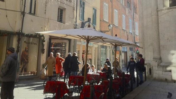 Une rue bordée de terrasses, de bâtiments et d’un édifice historique.