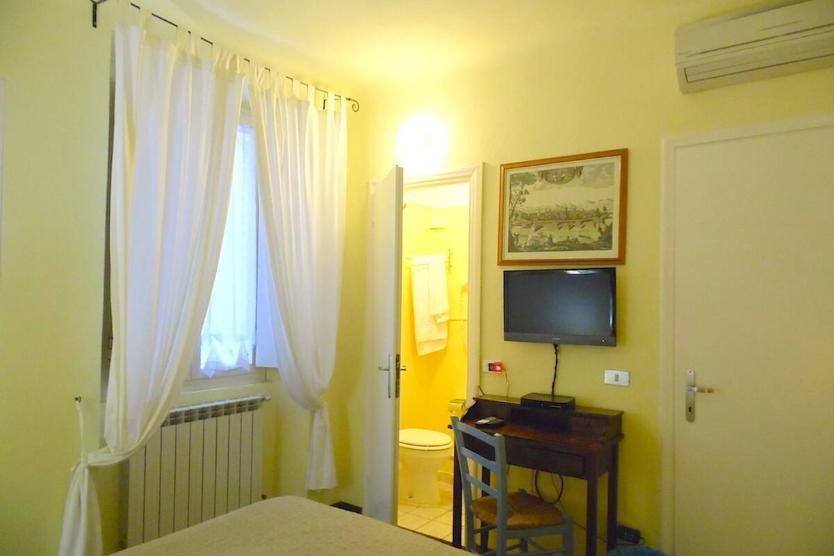 A small room with a bed, a desk with a computer, a television, and a window with curtains.