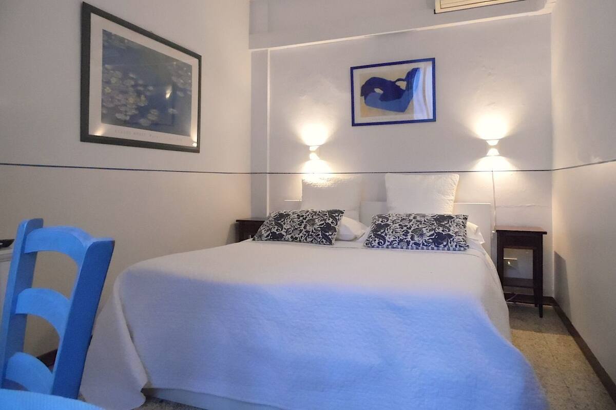 A bedroom with a bed, a chair, two wall-mounted lights, and two framed pictures.