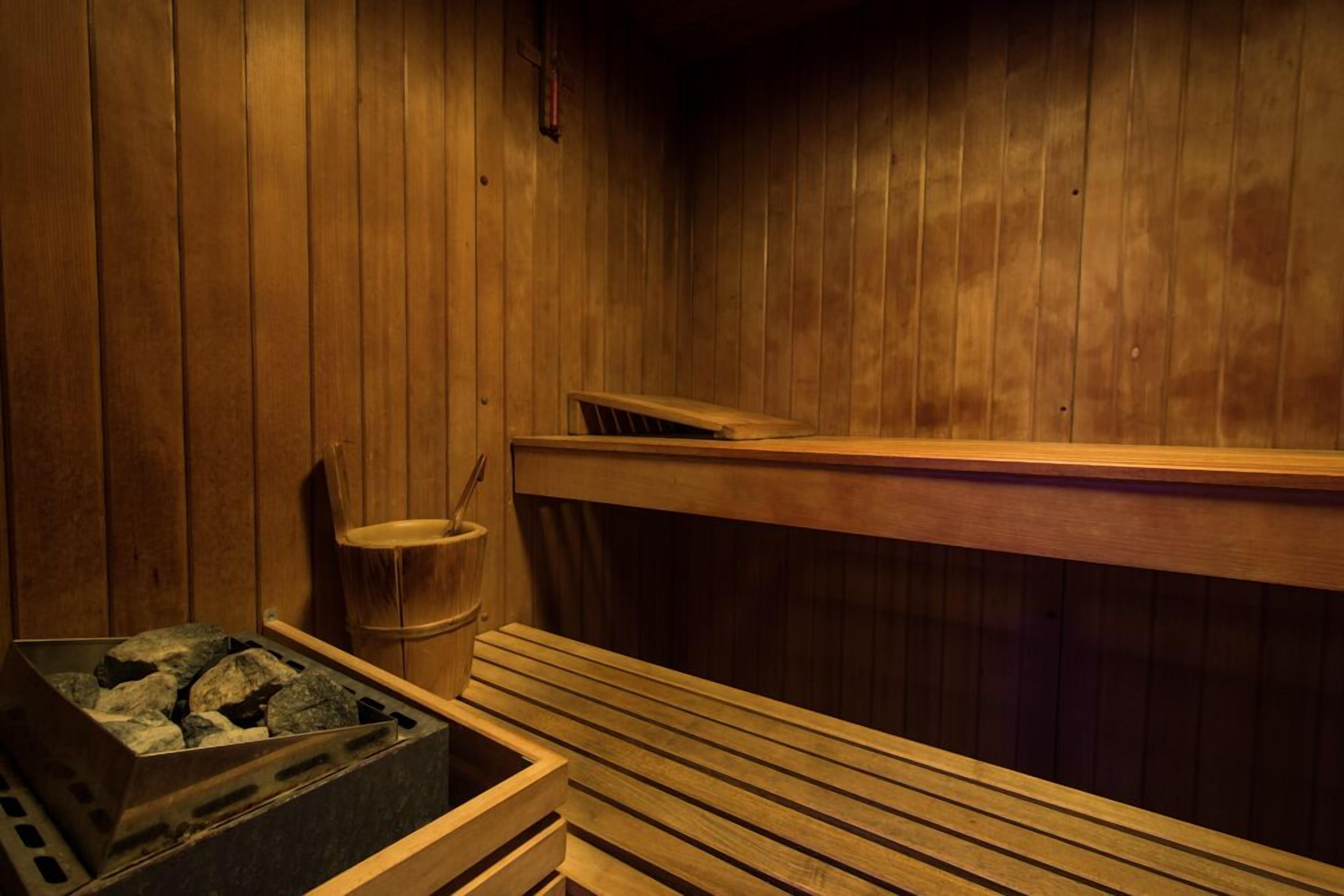 A sauna with wooden walls and benches, a bucket, and a container of stones.