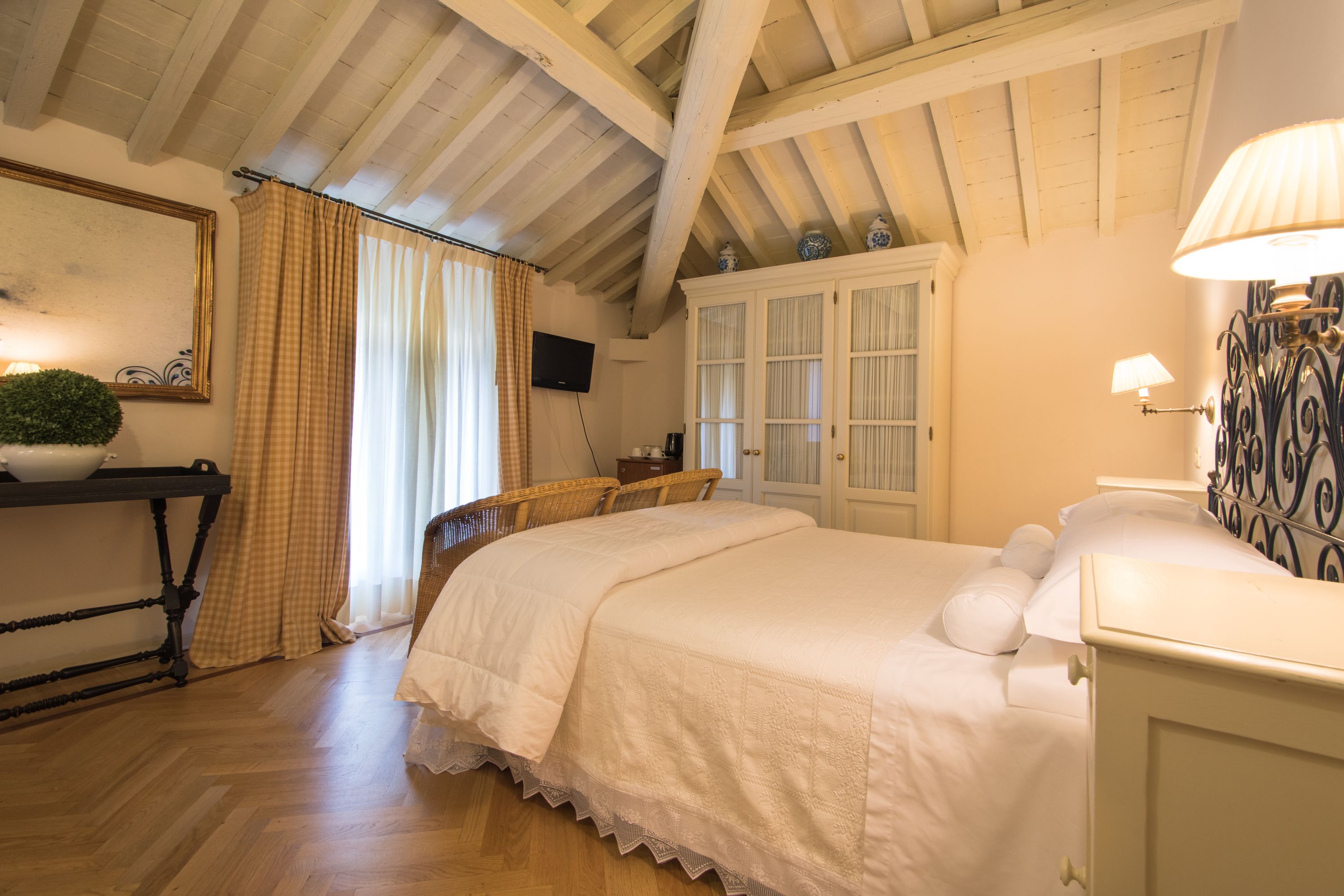 Ein Schlafzimmer mit Holzbalkendecke, einem Bett mit weißer Bettwäsche, einem Tisch mit Pflanze und einer Kommode mit Dekoration.