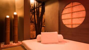 Un cuarto de spa con una cama, velas, una pared con un ventanal circular y un mural de un árbol.