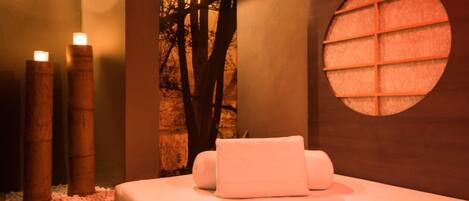 Un cuarto de spa con una cama, velas, una pared con un ventanal circular y un mural de un árbol.