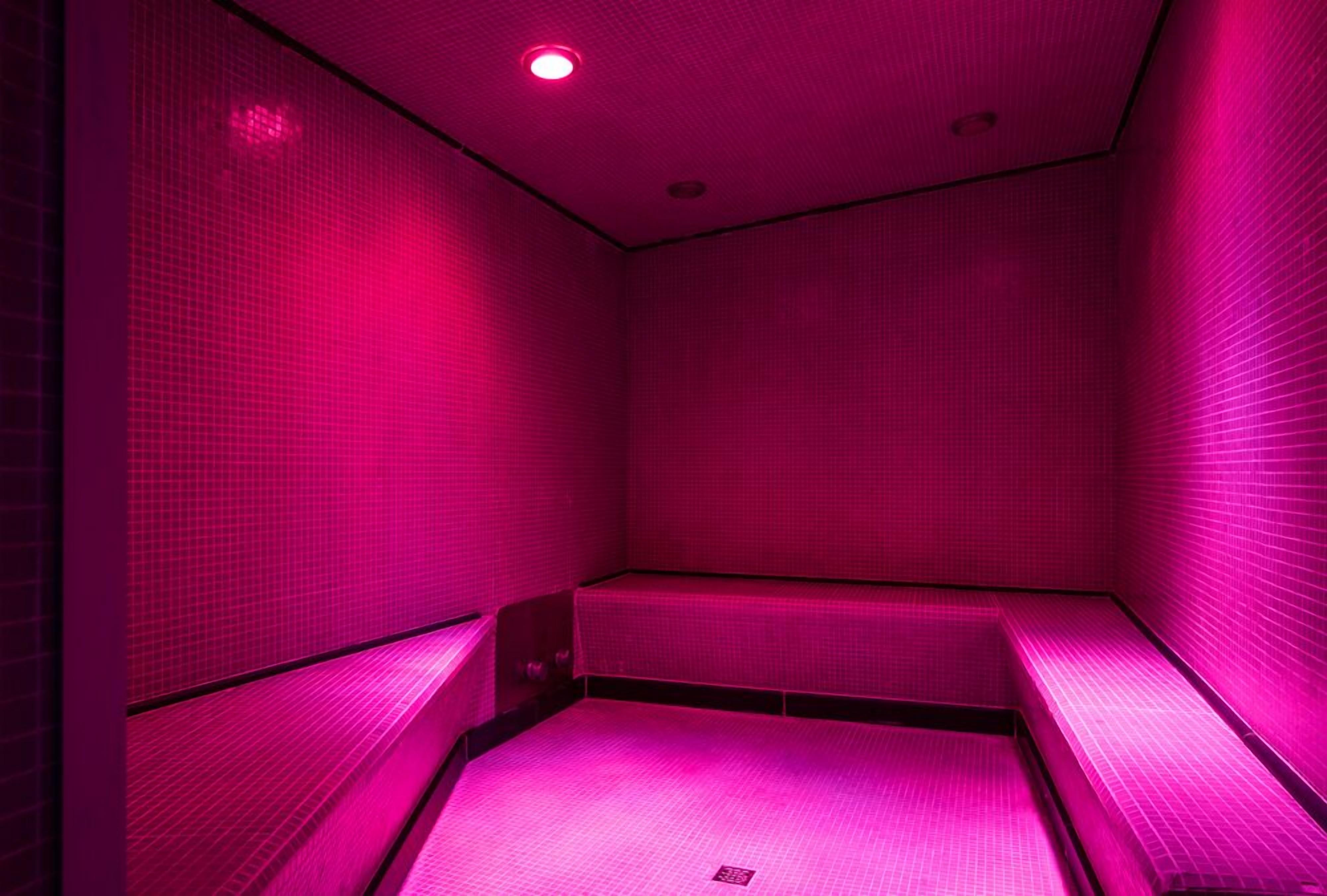 Une pièce à l’atmosphère chaleureuse, baignée d’une lumière rose, avec un banc le long d’un des murs et une petite table au centre.