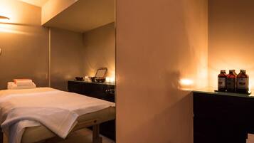 A hotel room with a bed, bedside table, and a small desk with bottles.