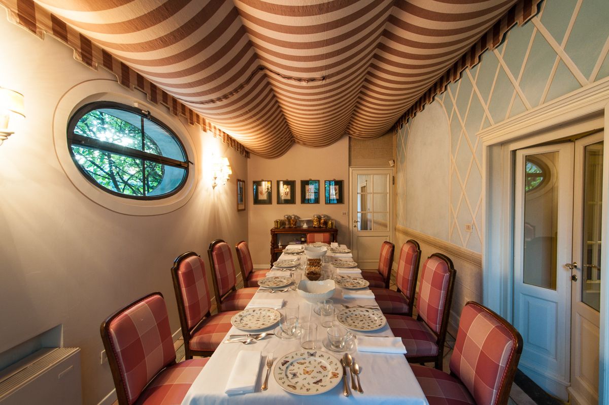 A dining room with a long table set for a meal, striped ceiling, and a window with a view of trees.