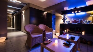 Un interno moderno con poltrone in vimini, un tavolo in legno con una candela e uno scaffale con barattoli e bottiglie.