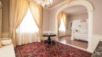 A room with a round table, clear chairs, a patterned carpet, and a bed with a canopy.