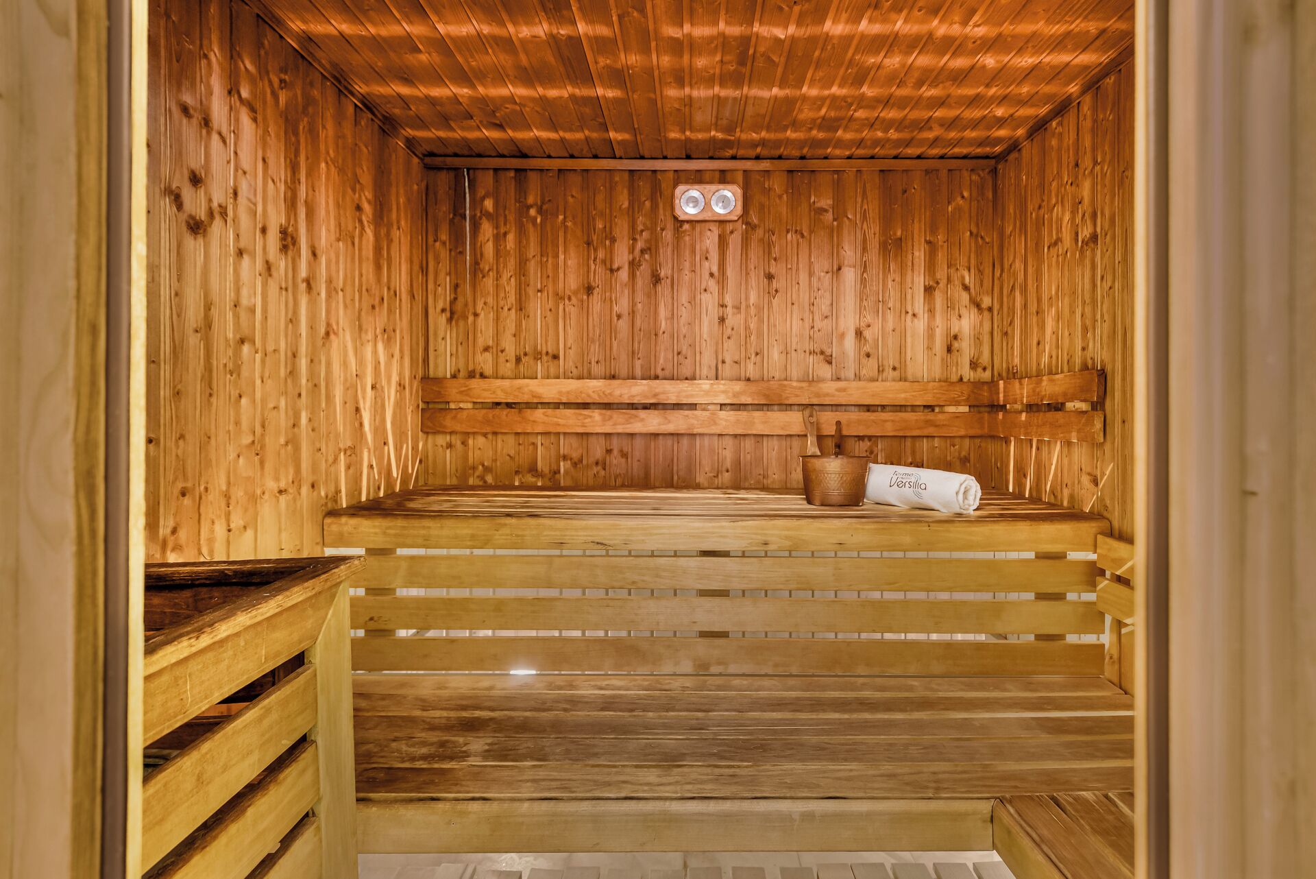 Una sauna in legno con panche, una seduta e un asciugamano, e una bacinella.