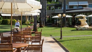 An outdoor patio area with wooden tables and chairs, surrounded by palm trees and a fountain. - Hotel Villa Undulna - Terme della Versilia (Montignoso)