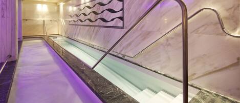A marble-lined pool with a glass bottom, a metal handrail, and a wavy pattern on the wall.
