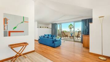 Uma sala de estar moderna com sofá azul, piso de madeira, porta de vidro que dá para uma varanda e um quadro na parede.