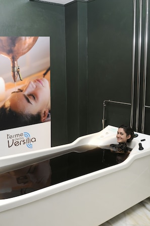 A spa area with a white bathtub and a poster advertising 'Termini della Versilia'.