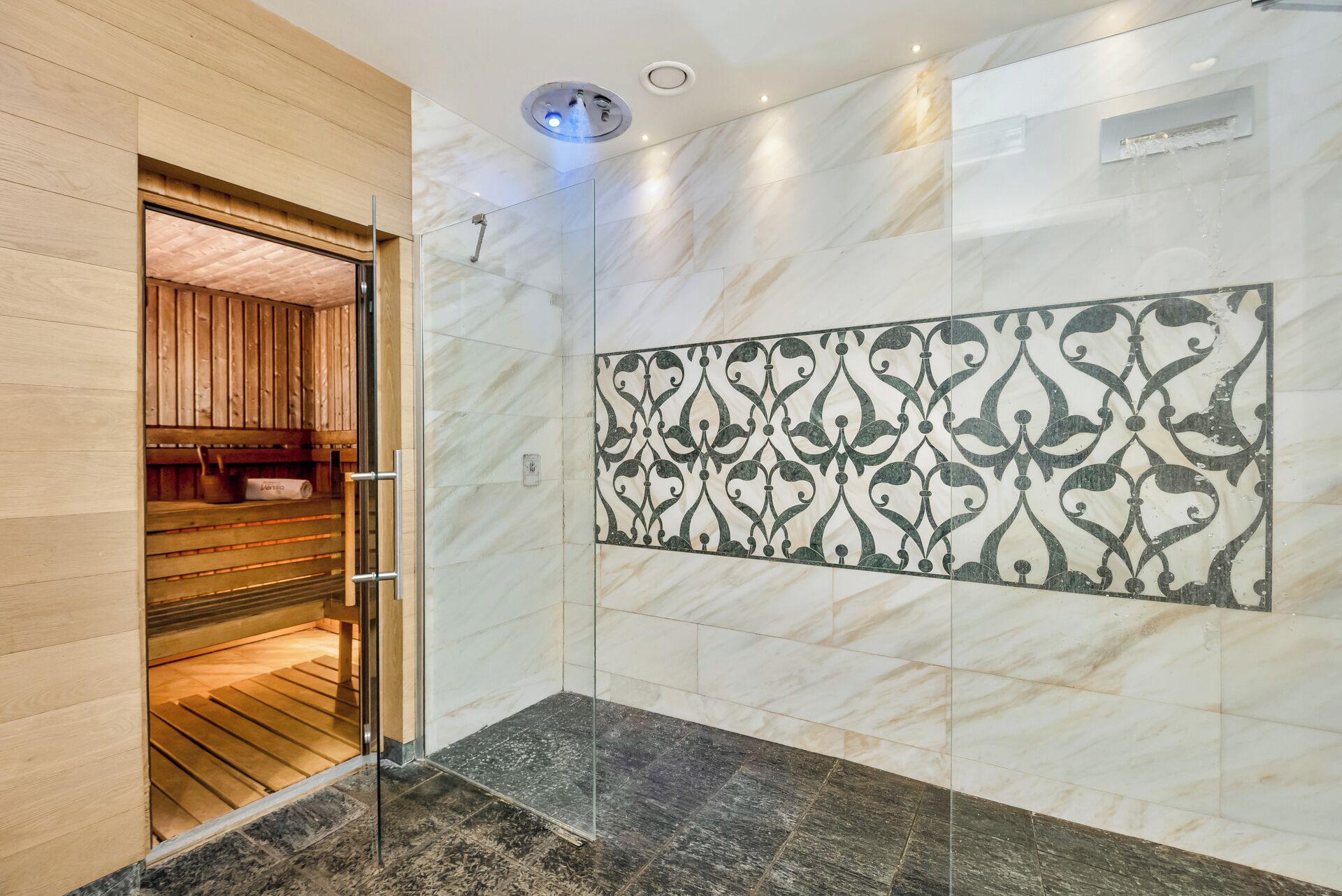 A modern bathroom with a glass shower enclosure, marble walls, and a wooden bench.