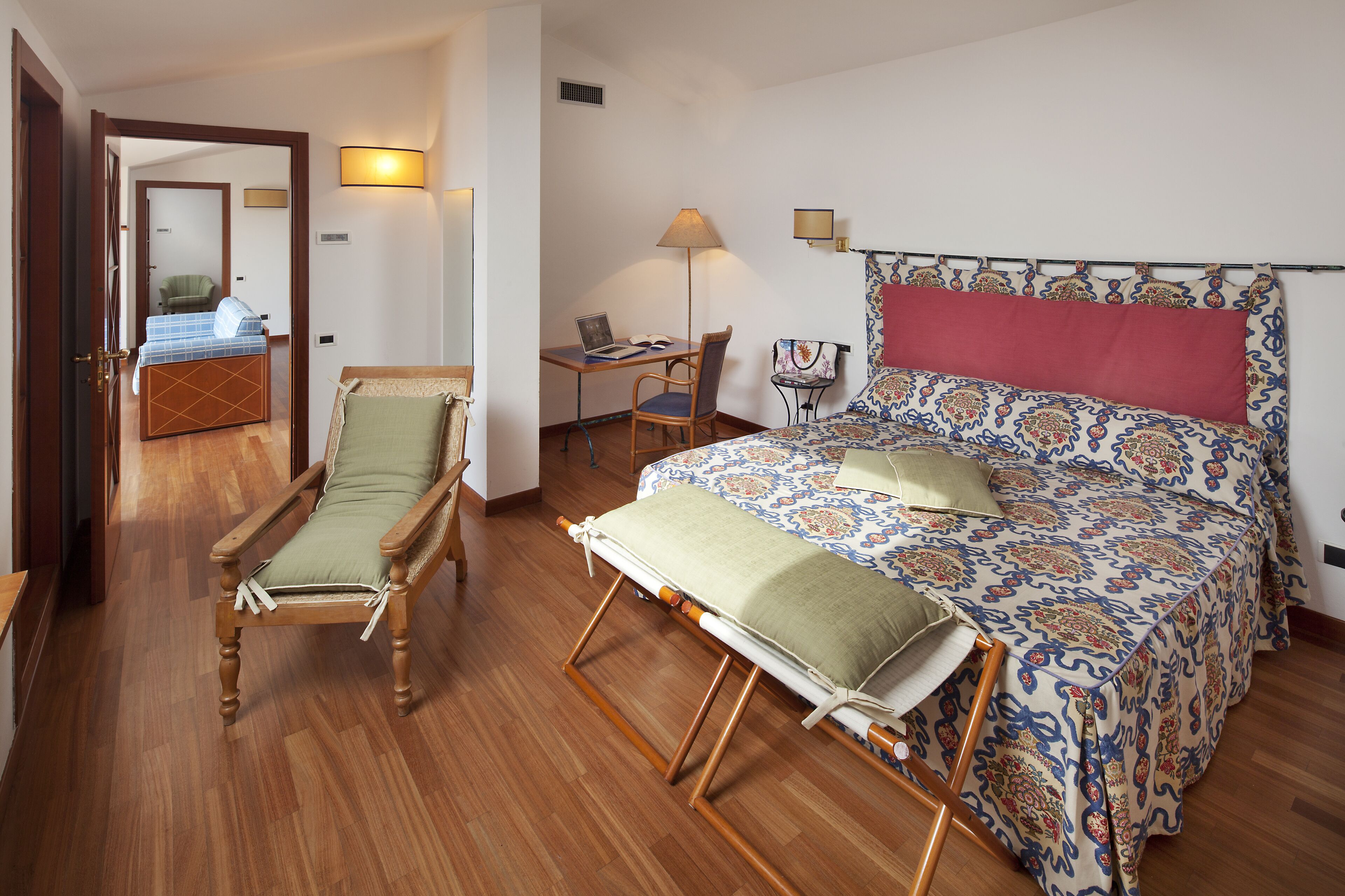 A bedroom with a bed, a desk, a chair, and a bedside table.