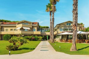 A hotel with a central pathway leading to a covered outdoor seating area, surrounded by palm trees and greenery. - Hotel Villa Undulna - Terme della Versilia (Montignoso)