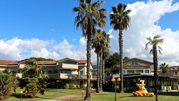 A hotel with multiple-story buildings, palm trees, and a well-maintained lawn. - Hotel Villa Undulna - Terme della Versilia (Montignoso)