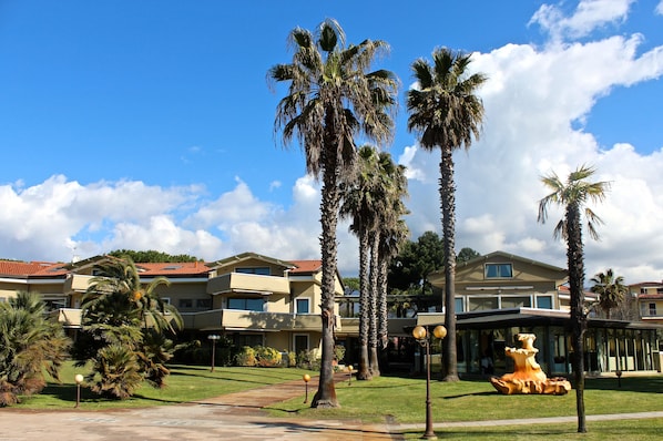Un hotel con edificios de varios pisos, palmeras y un césped cuidado.
