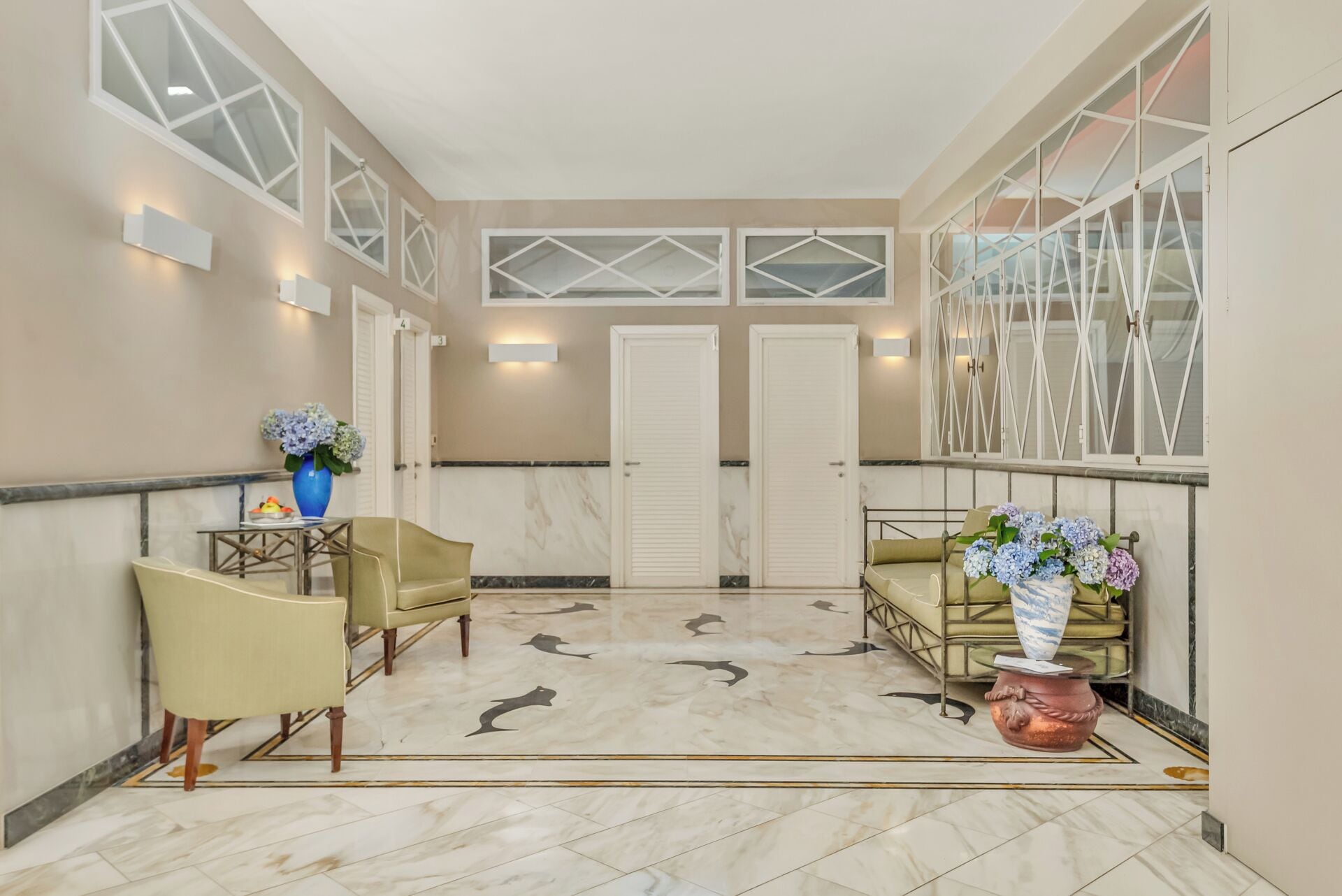 Una hall con pavimento in marmo, due divani, un vaso con fiori e un punto luce a parete.