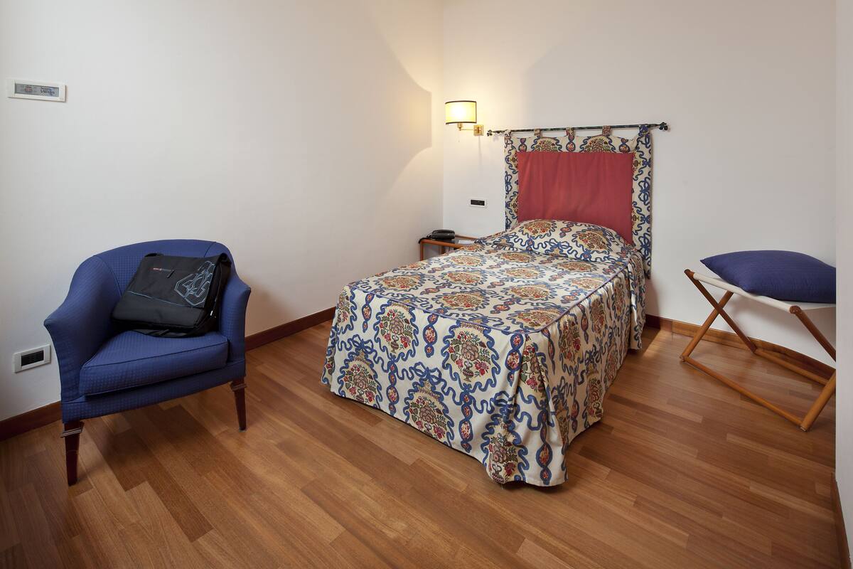 Una camera da letto con un letto, una poltrona blu, un pavimento in legno e un comodino.