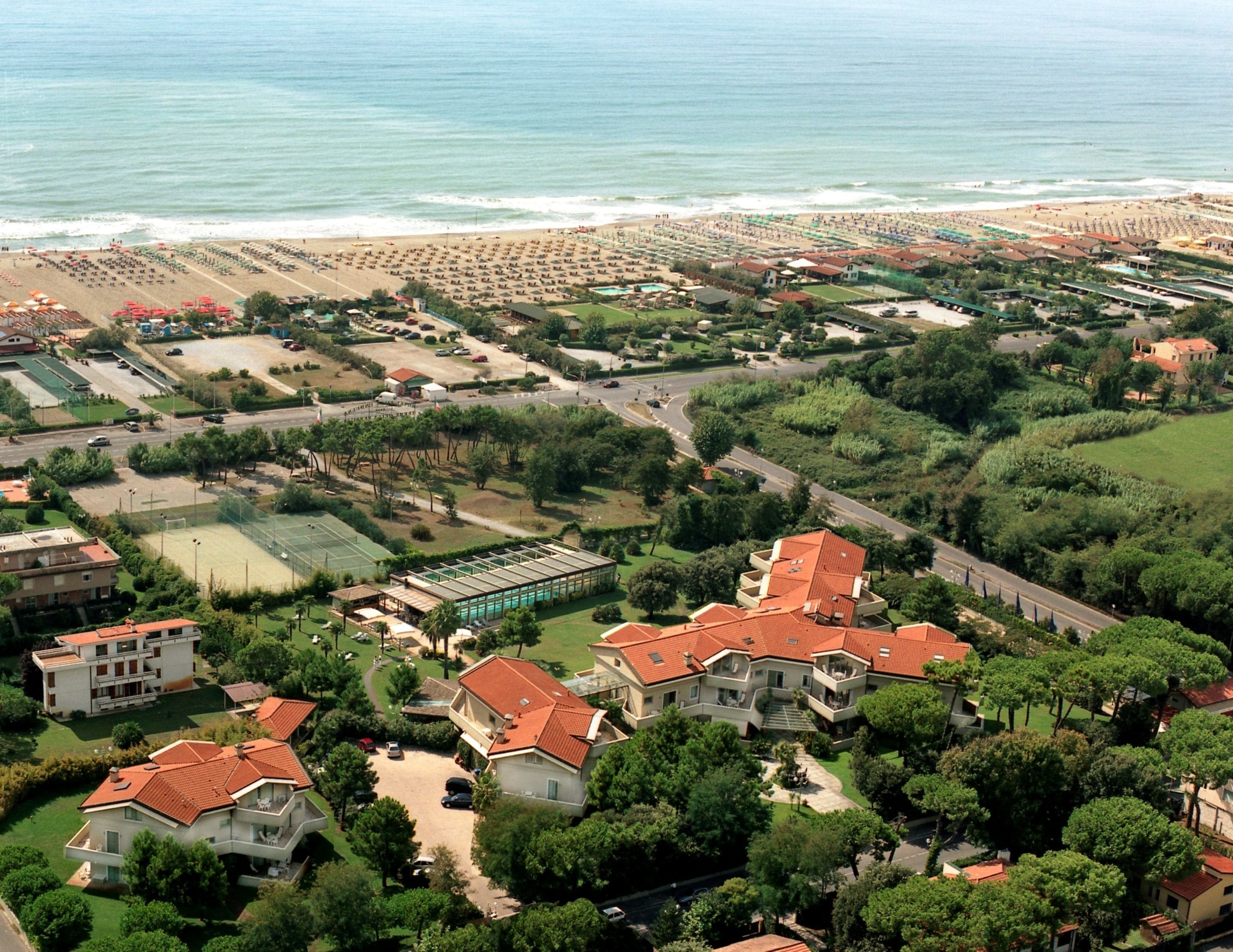 An aerial view of a coastal residential area with houses, a beach, and a swimming pool complex.