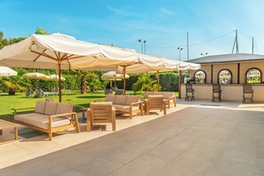 Eine Terrassengruppe im Freien mit Holzmöbeln, beigen Kissen und großen Sonnenschirmen.
