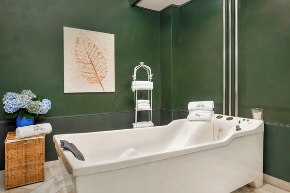 A modern bathroom with a freestanding bathtub, a towel rack, and a decorative leaf painting on the wall.