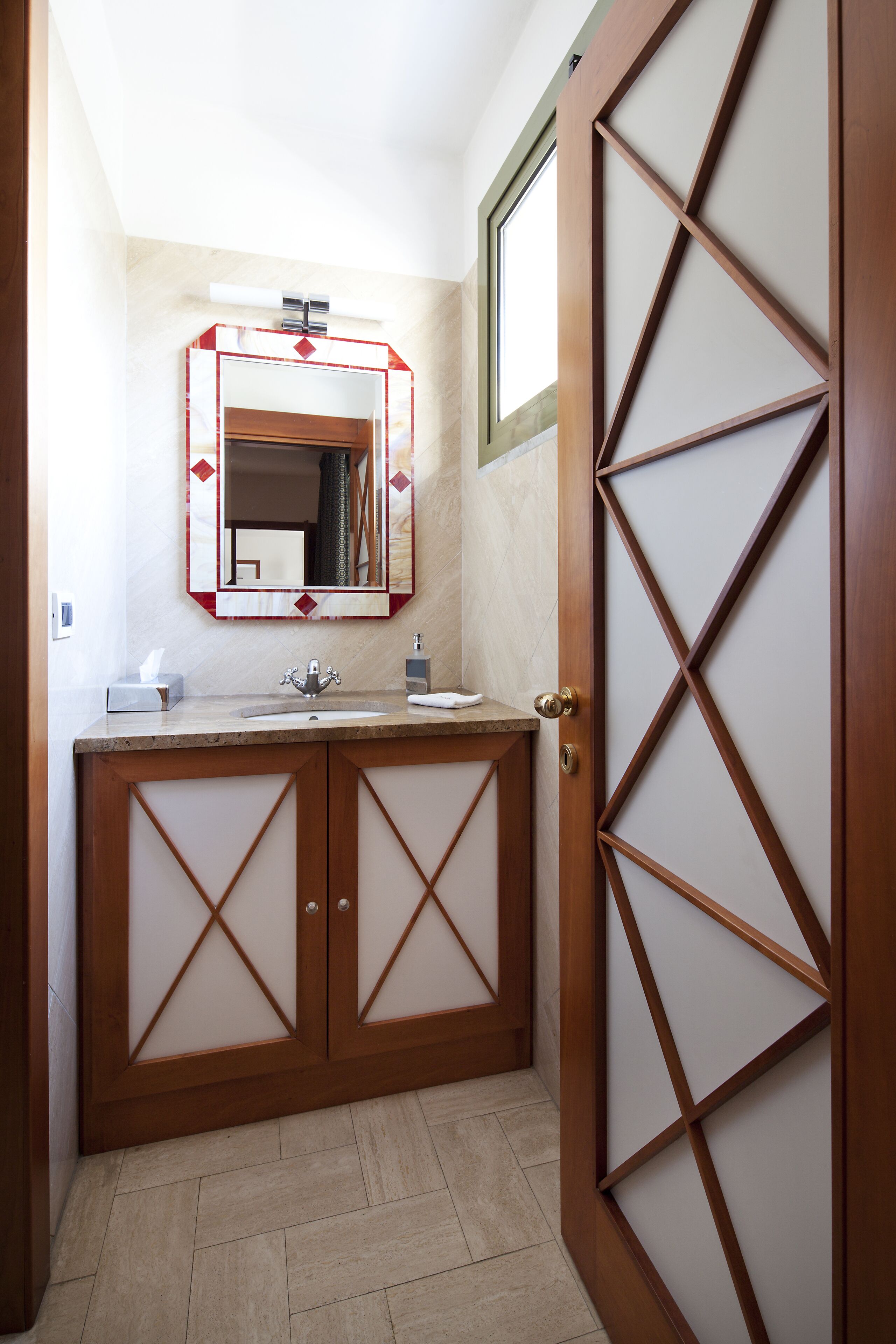 A bathroom with a wooden vanity, a mirror with a decorative frame, and a door with a geometric pattern.