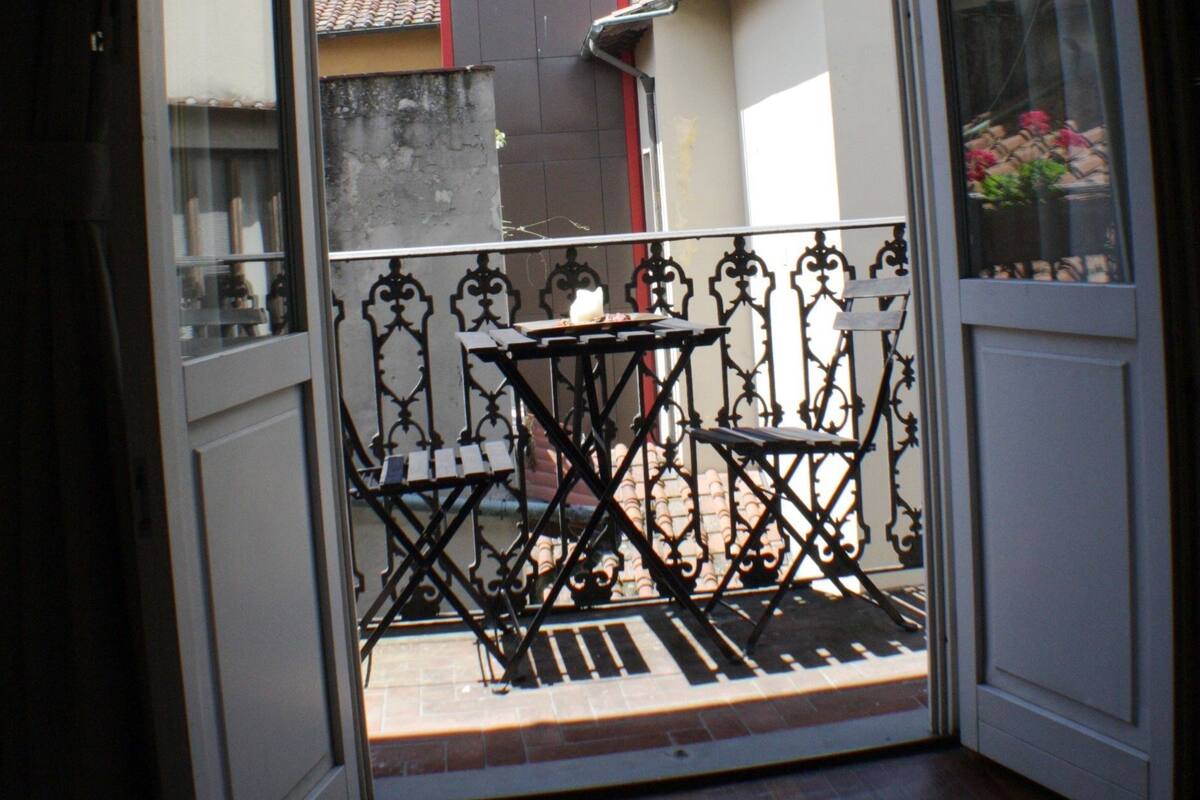 Un balcon avec une table et des chaises, une vue sur un bâtiment doté d’un clocher et un ciel dégagé.