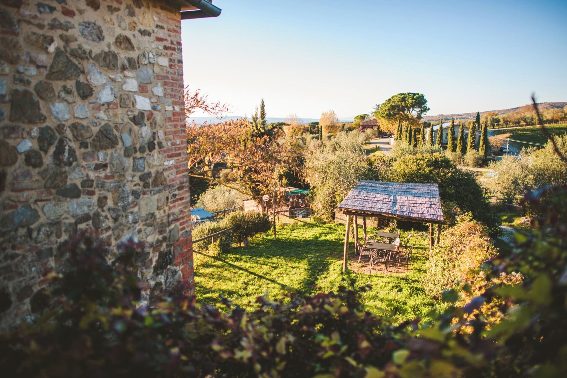 A stone building with a rustic roof structure in a lush garden.