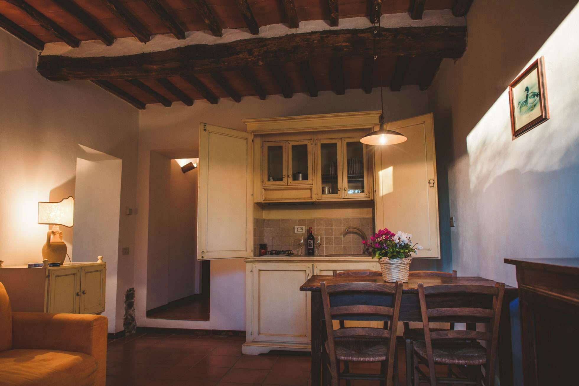 Una cucina accogliente con mobili in legno, un tavolo da pranzo con sedie e un vaso di fiori.